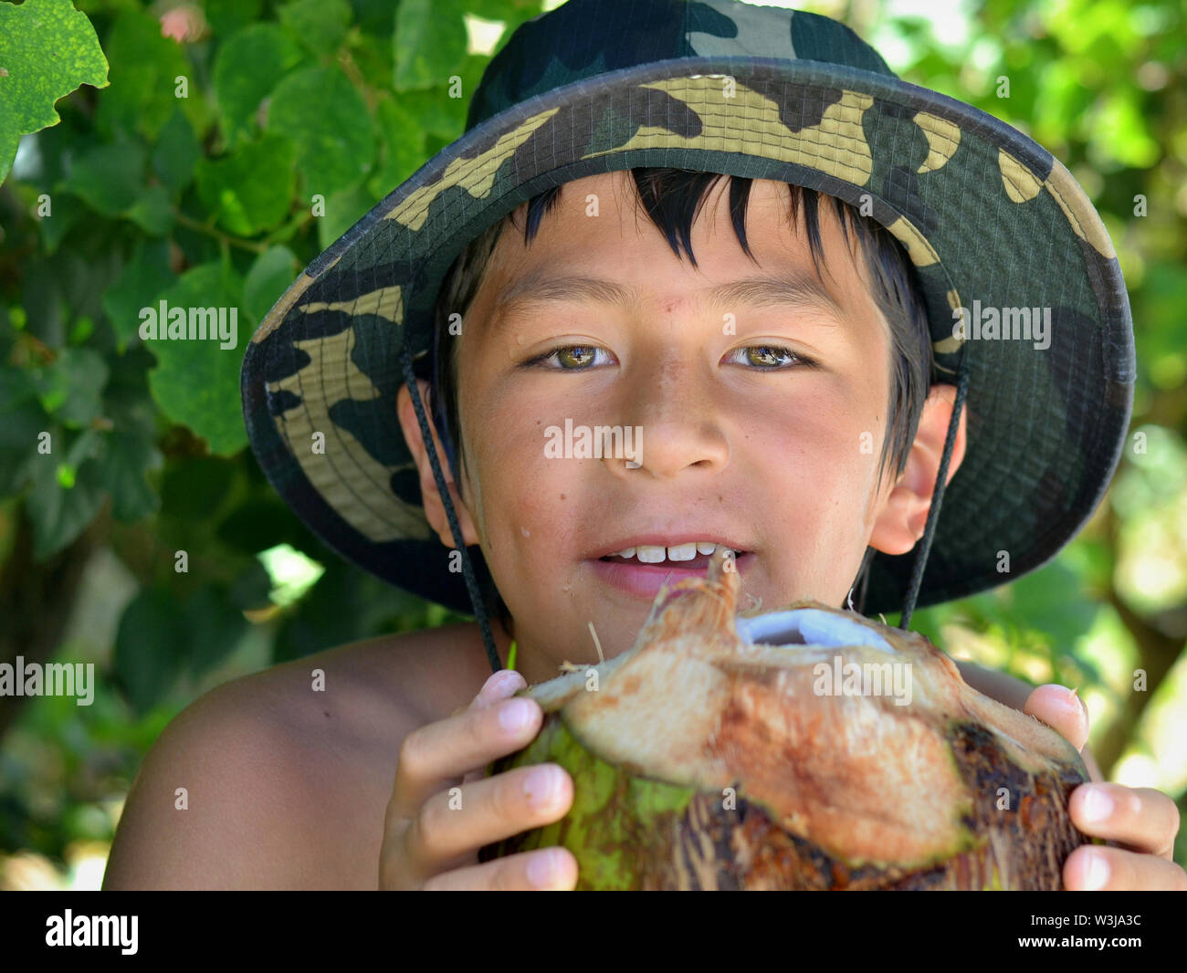 Cute Kanadischen gemischten Rennen Junge (Kaukasische und Südostasiatischen) auf Ferien in Kuba hält eine frische Kokosnuss mit beiden Händen. Stockfoto