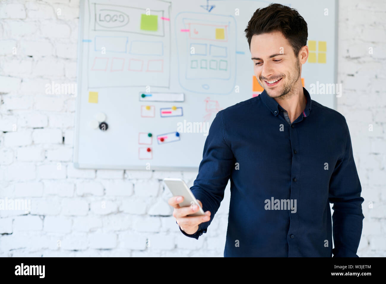 Happy Web Designer suchen auf seinem Smartphone im Büro Stockfoto