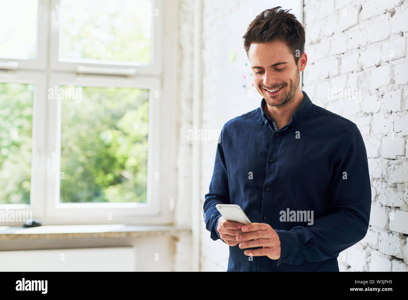 Glückliche junge Mann mit seinem Smartphone im Büro Stockfoto