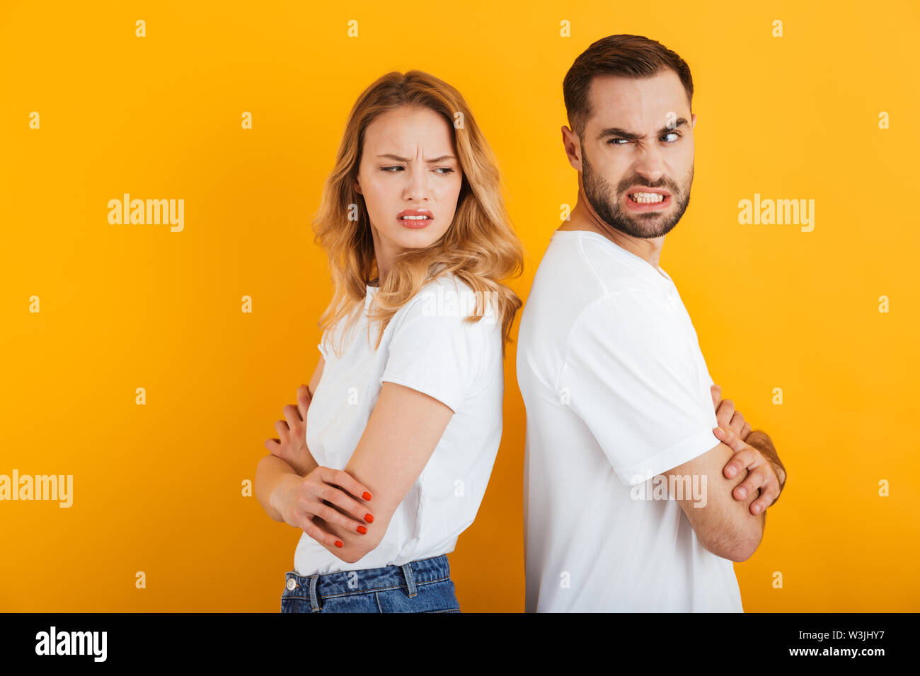 Bild von wütenden Menschen, Mann und Frau in Basic t-shirts runzelte die Stirn, während sie sich im Kampf um einen gelben Hintergrund isoliert zurück Stockfoto