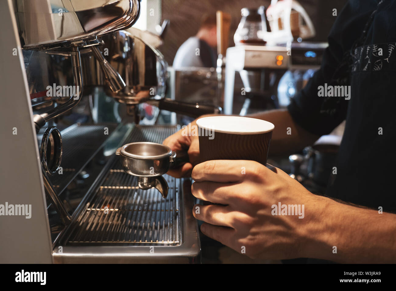 Barista Mann mit heißem Kaffee trinken in Papier Schale in der einen Hand und Kaffee Inhaber in einem anderen in der Nähe von professionelle Kaffeemaschine in Nahaufnahme Stockfoto