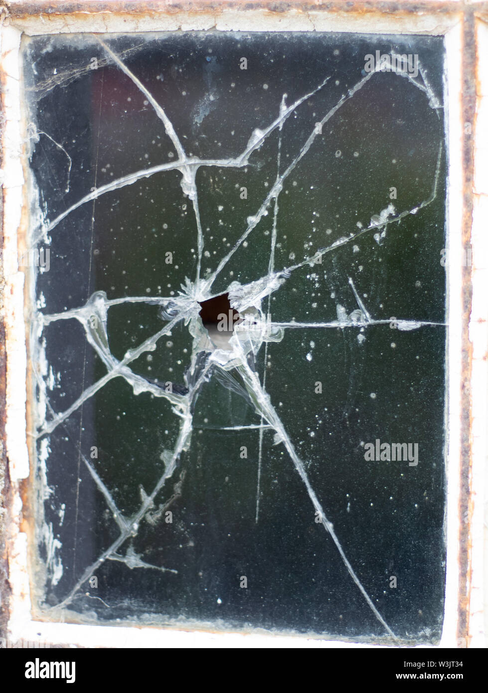 Ein einschußloch in einem Fenster der alten, dreckigen Glas in einer verlassenen und verfallenen Lager Stockfoto