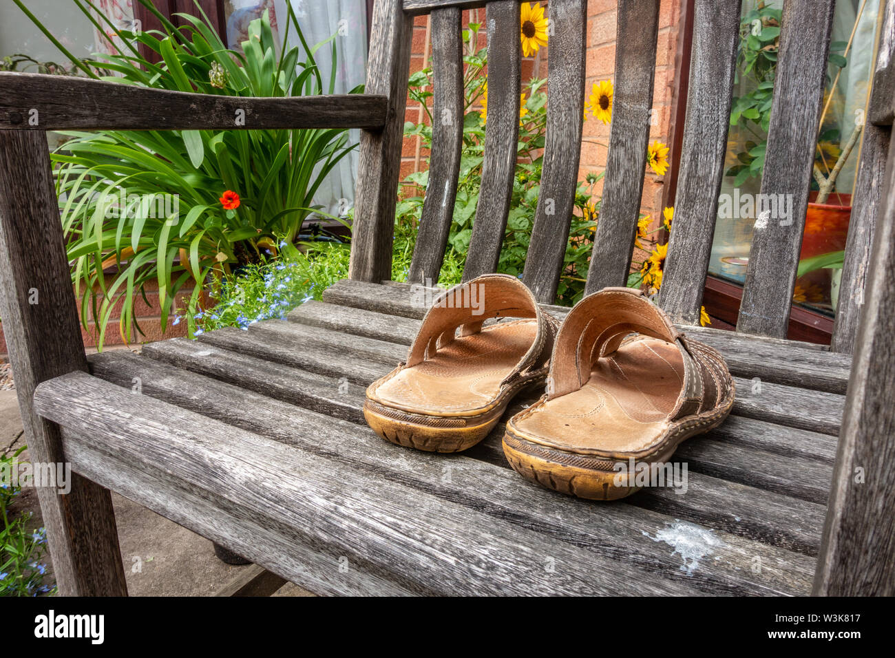 Ein paar Sandalen aus Leder für Männer auf einer hölzernen Sitz in einem Garten. Stockfoto
