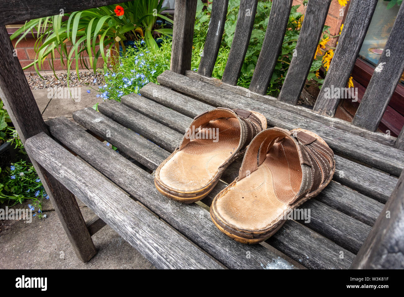 Ein paar Sandalen aus Leder für Männer auf einer hölzernen Sitz in einem Garten. Stockfoto
