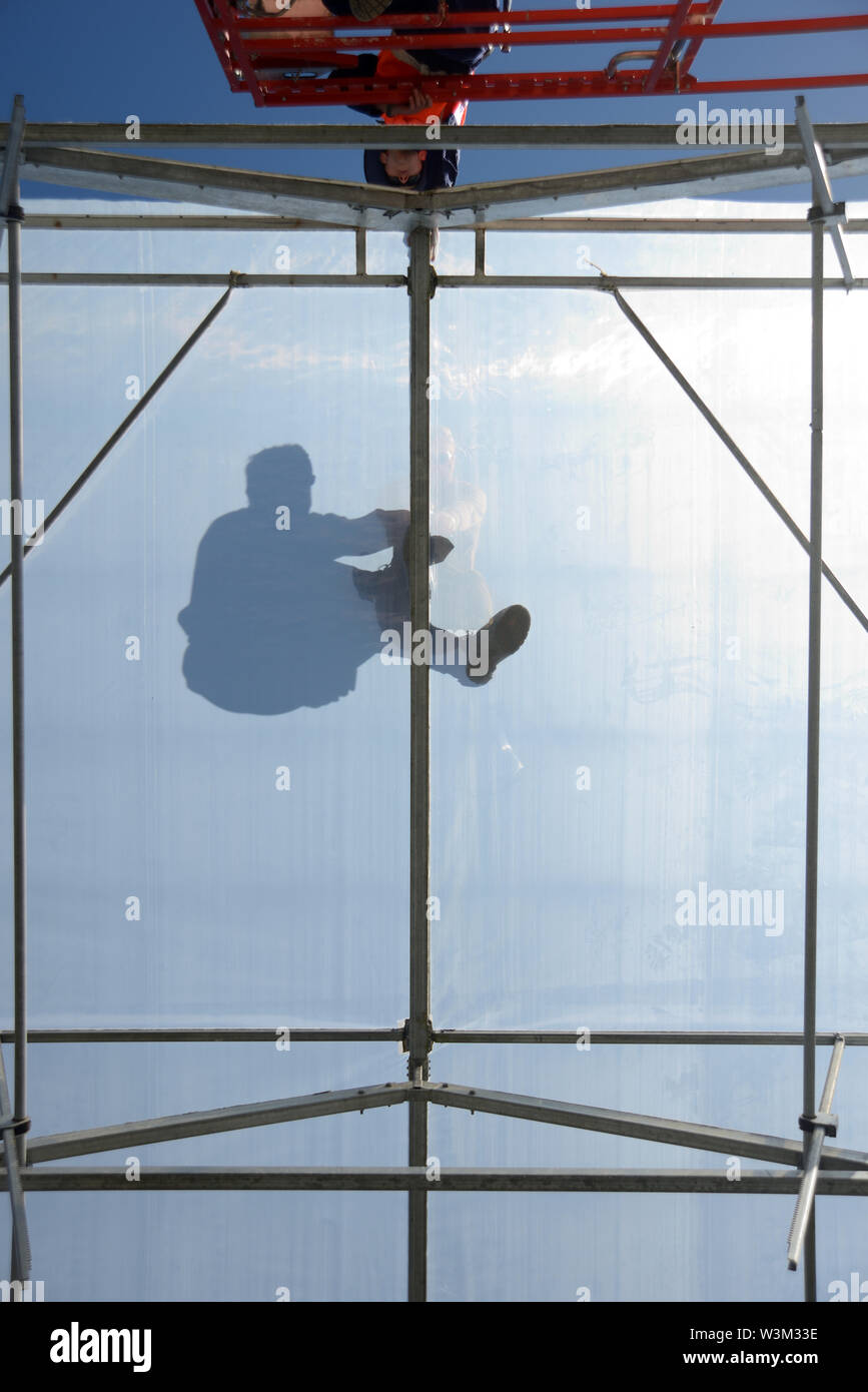 Greymouth, Neuseeland, Dezember 12, 2018: ein Kaufmann in Silhouette gesehen, so wie er sichert die Plastik auf dem Kamm eines Tunnel House. Stockfoto