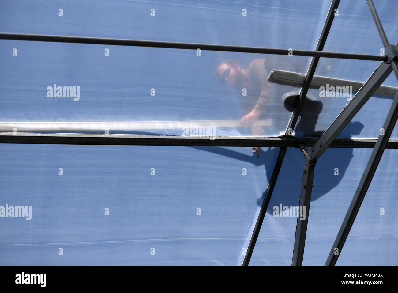 Greymouth, Neuseeland, 12. Dezember 2018: Kaufmann in Silhouette gesehen, so wie er den Kunststoff auf dem Kamm eines Tunnel House befestigt ist. Stockfoto