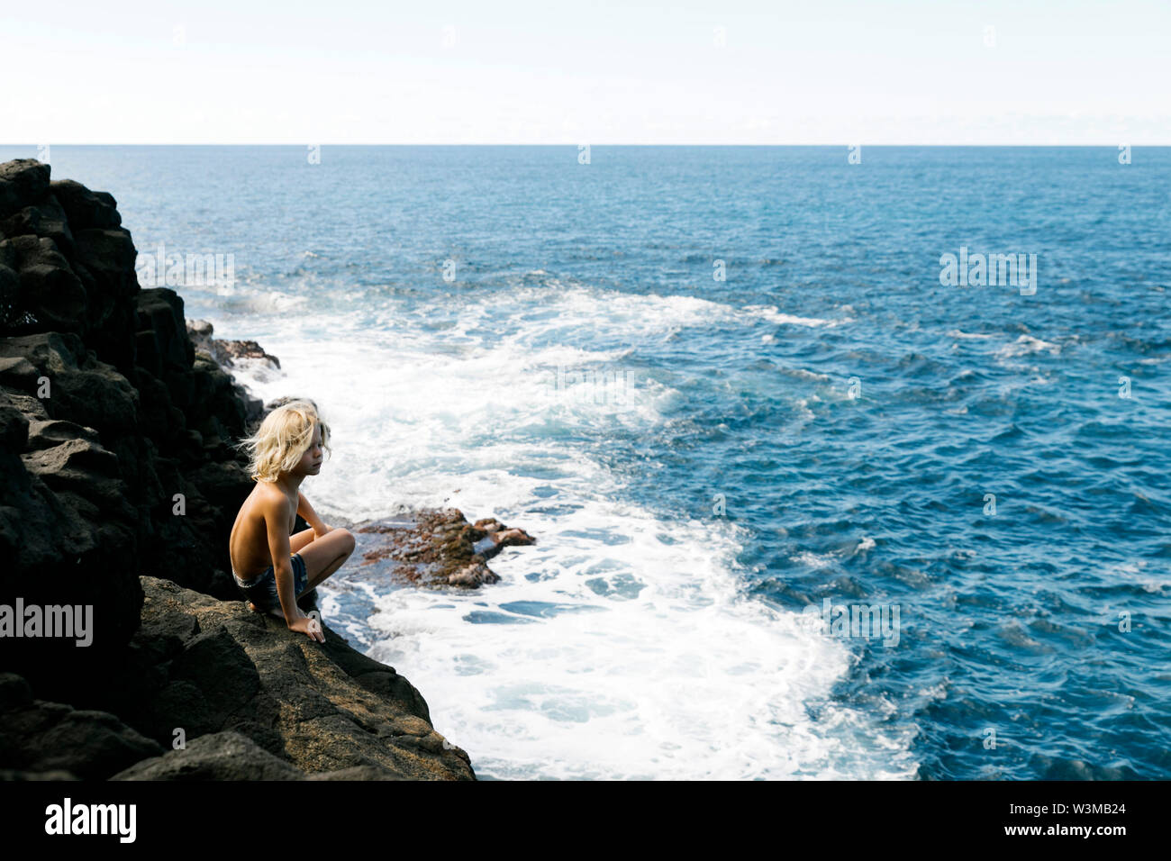 Junge zusammengekauert auf der Klippe von Meer Stockfoto