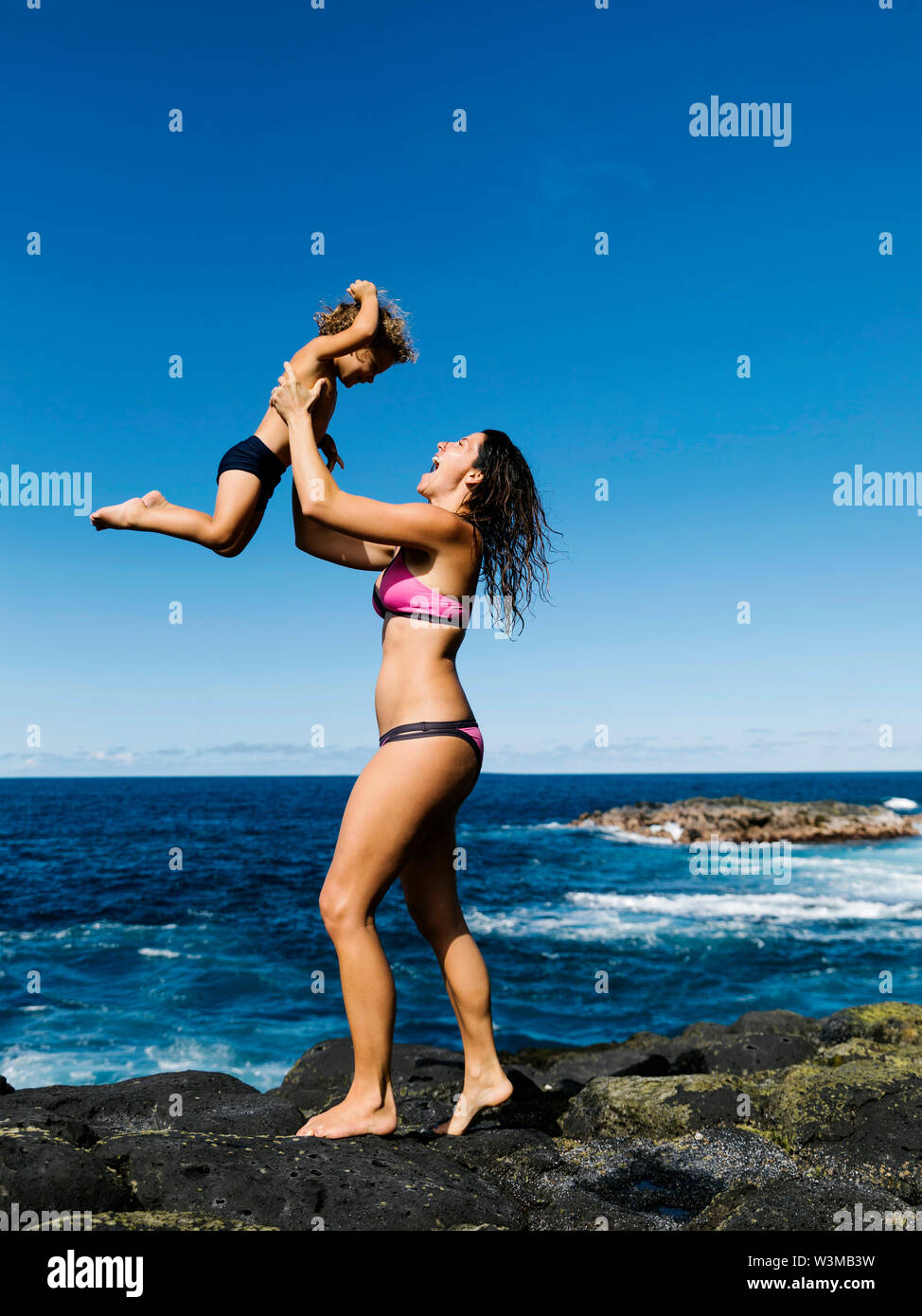 Die Mutter ihren Sohn auf Felsen Anheben durch Meer Stockfoto