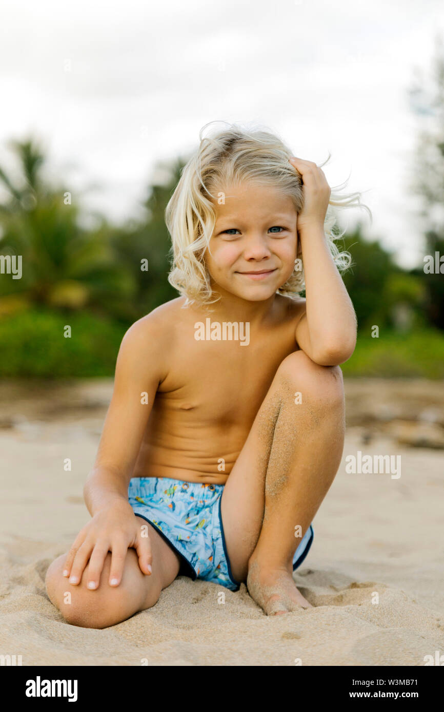 Blonde Junge kniend am Strand Stockfoto