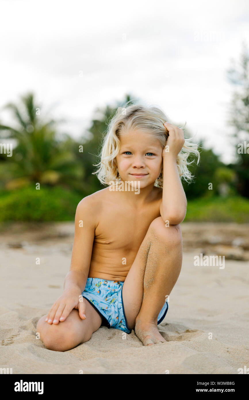 Blonde Junge kniend am Strand Stockfoto