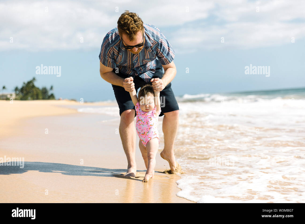 Vater, der sein Baby girl Spaziergang am Strand helfen Stockfoto
