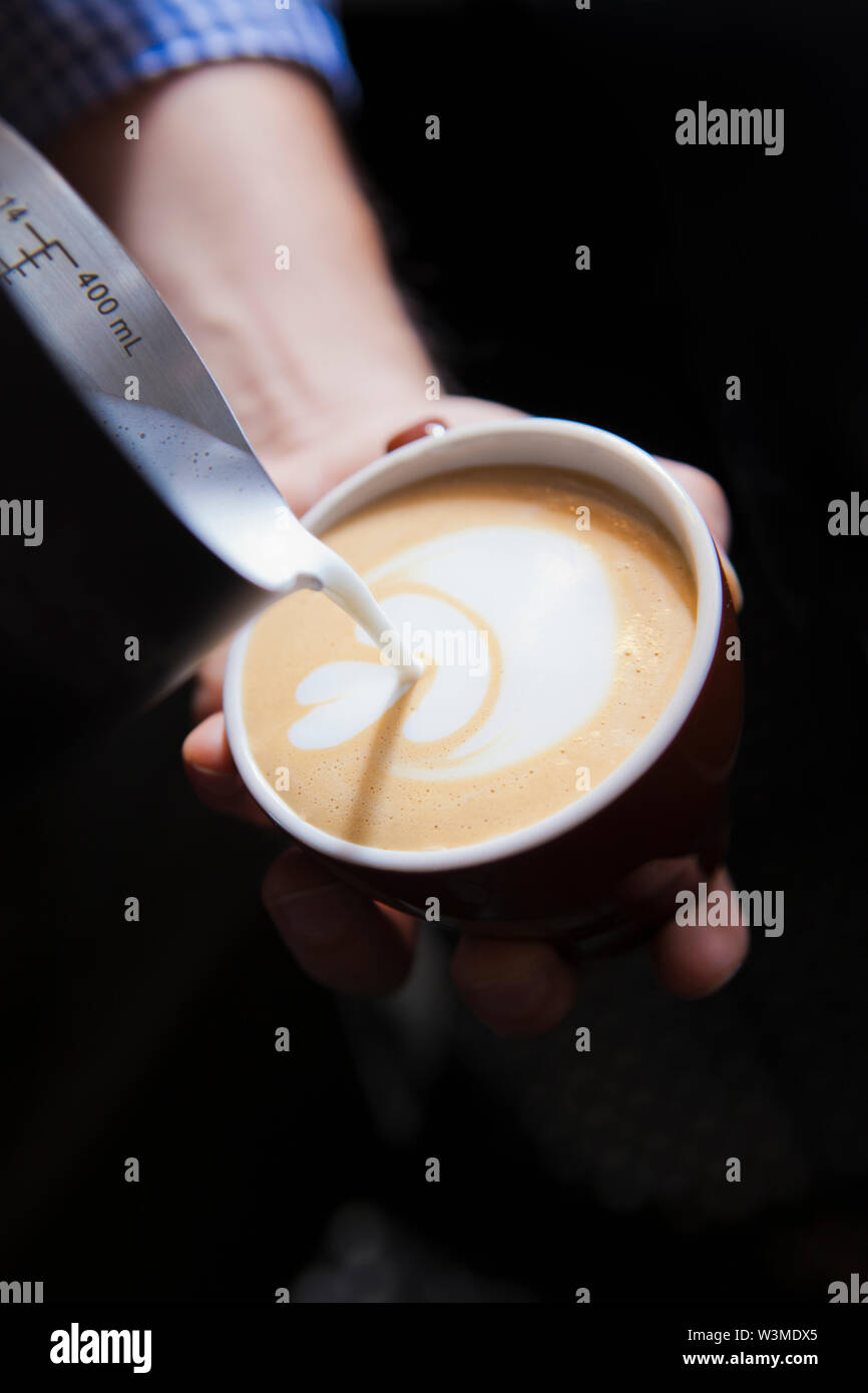 Barista gießen Milch in Kaffee Stockfoto