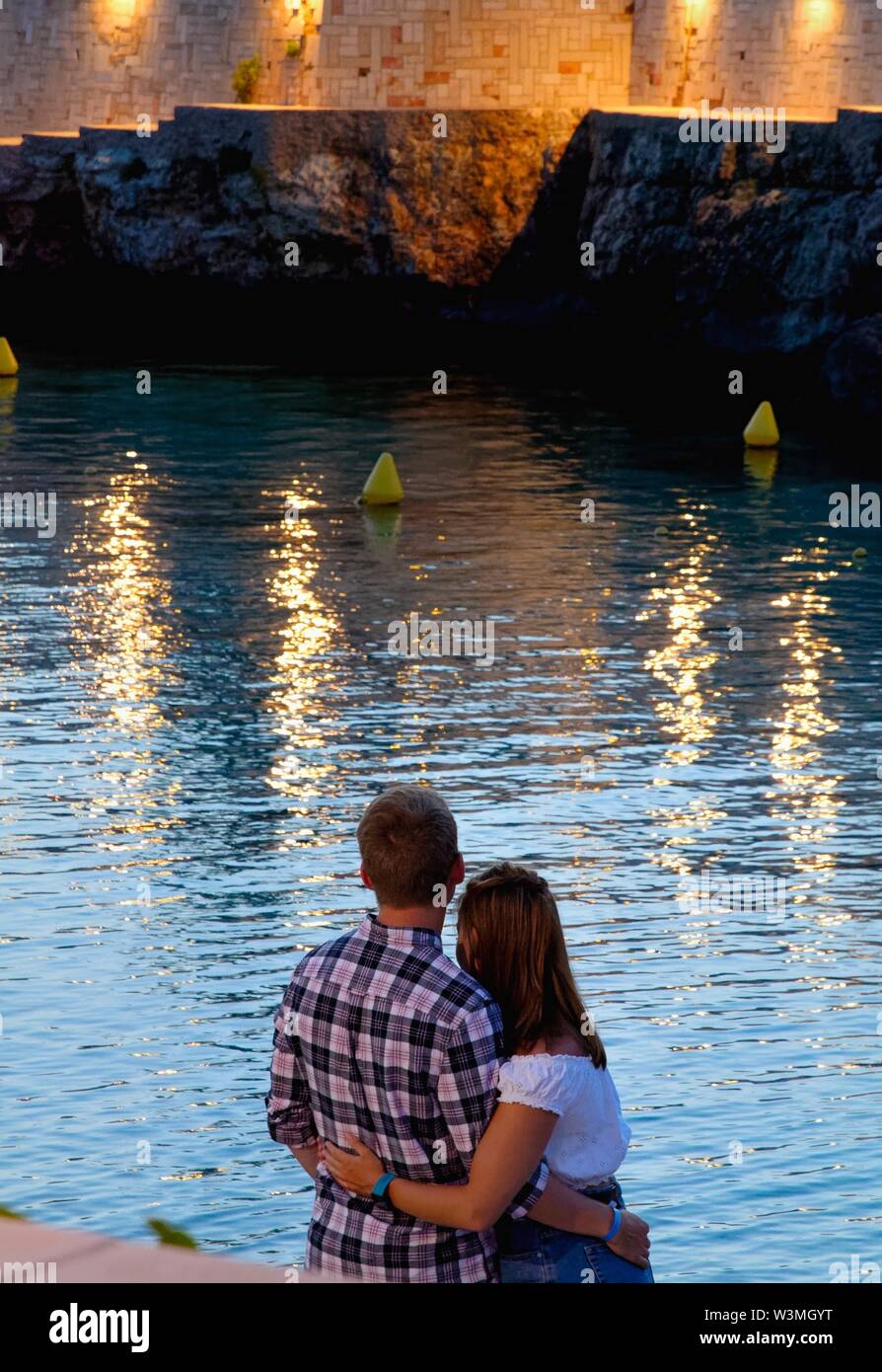 Rückansicht eines jungen Paares, das an der bunten Reflexion auf das Meer am Strand von Cala Blanca in der Nacht Ciutadella Menorca Spanien Europa Stockfoto