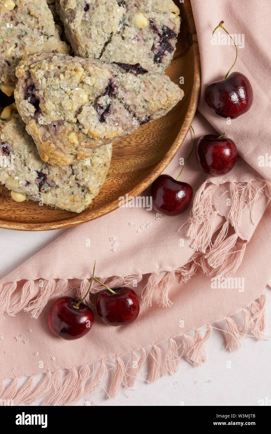 Kirsch- und weißer Schokolade Scones auf einer Holzplatte mit einem rosa Serviette und Kirschen vertikale Stockfoto