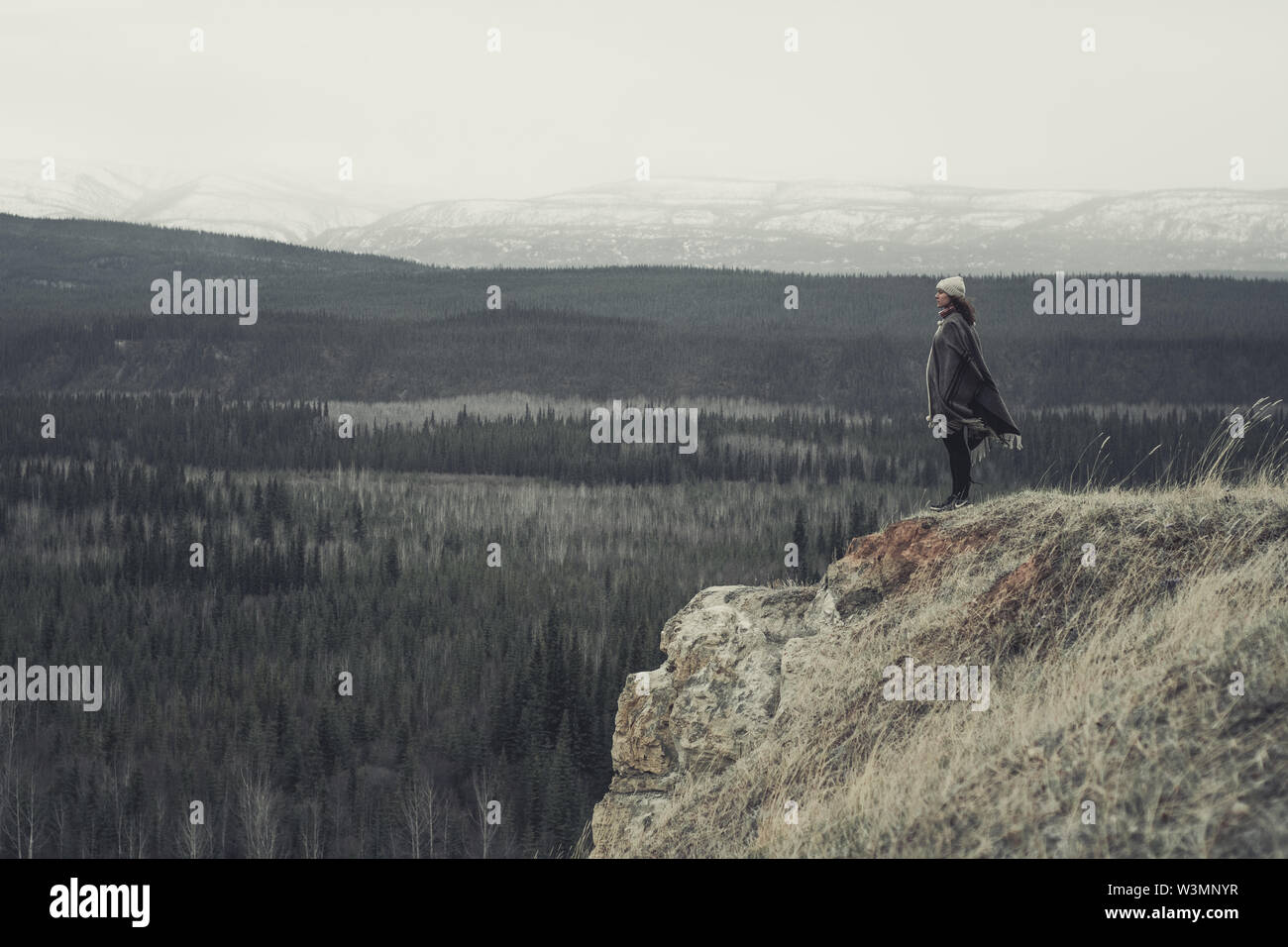 Eine junge Frau steht am Rand einer Klippe mit einer endlosen Blick auf Wald und Berge. Yukon Territory, Kanada Stockfoto