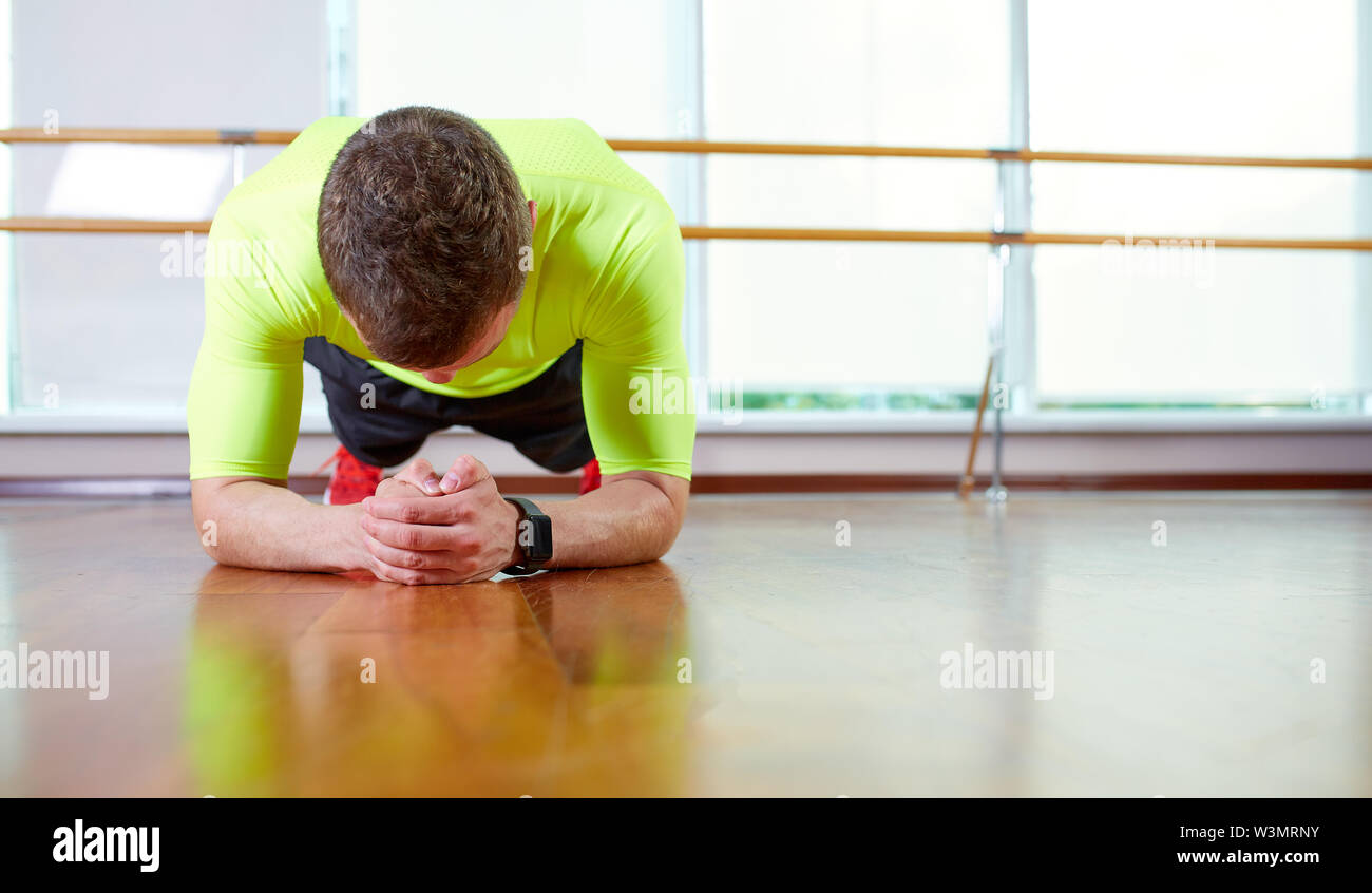 Es Plank zuversichtlich muskulösen jungen Mann mit Sport Verschleiß und tun Ganzkörperstütz während des Trainings auf dem Boden im Loft Innenraum Stockfoto