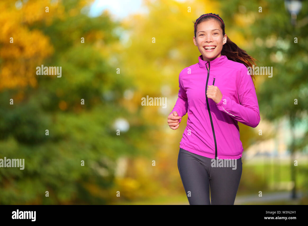 Weibliche Jogger. Passen junge asiatische Frau Joggen im Park lächelte glücklich und genießen Sie einen gesunden Lebensstil im Freien. Fitness runner Mädchen im Herbst Wald mit Herbst Laub. Gemischte Rasse asiatischen Kaukasischen. Stockfoto
