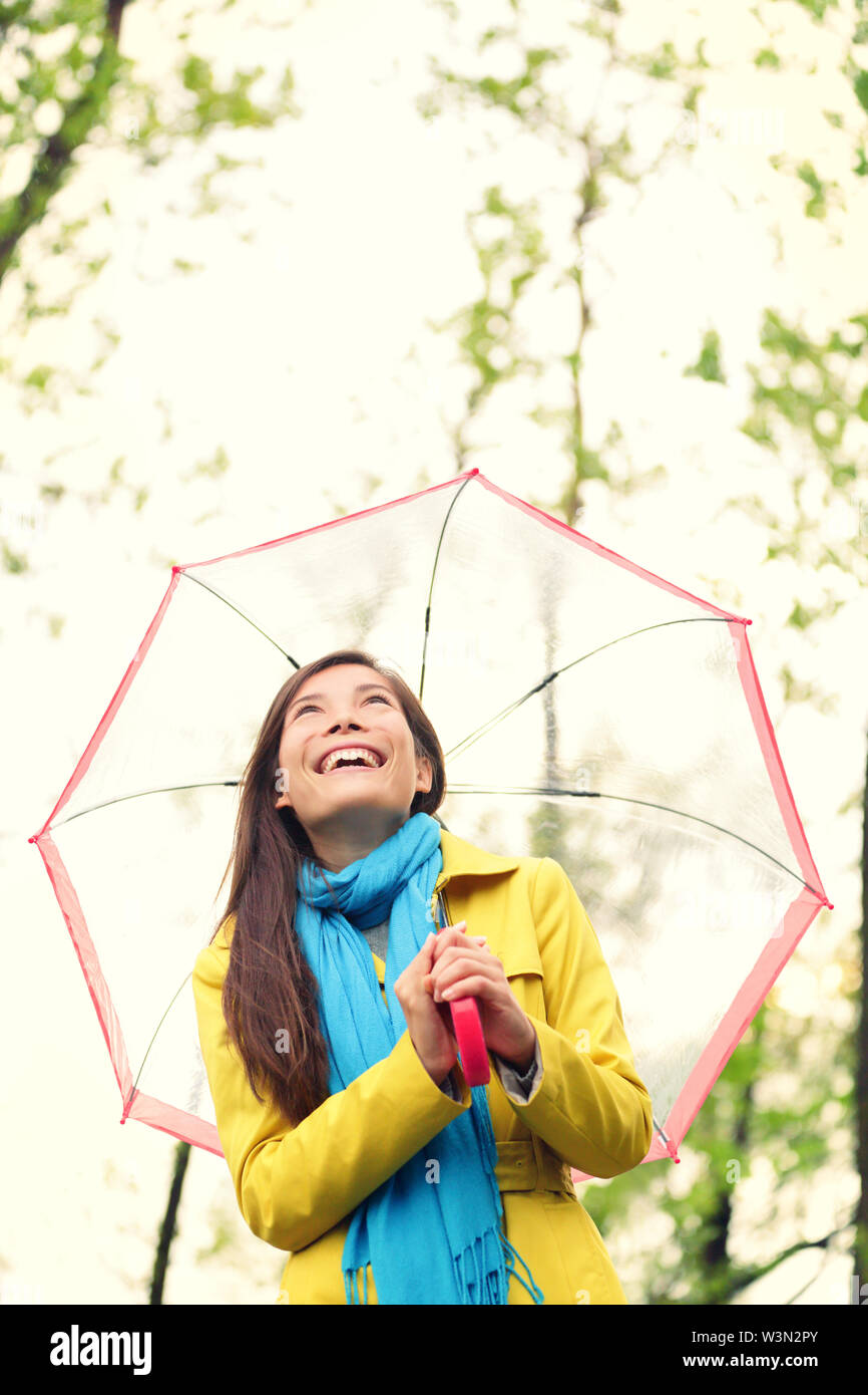 Asiatische Frau im Herbst mit Schirm im Regen freuen. Weibliche Modell zu Clearing Himmel Freude an regnerischen Herbst Tag tragen gelbe Regenmantel in der freien Natur Wald am See. Mischlinge asiatisches Mädchen. Stockfoto