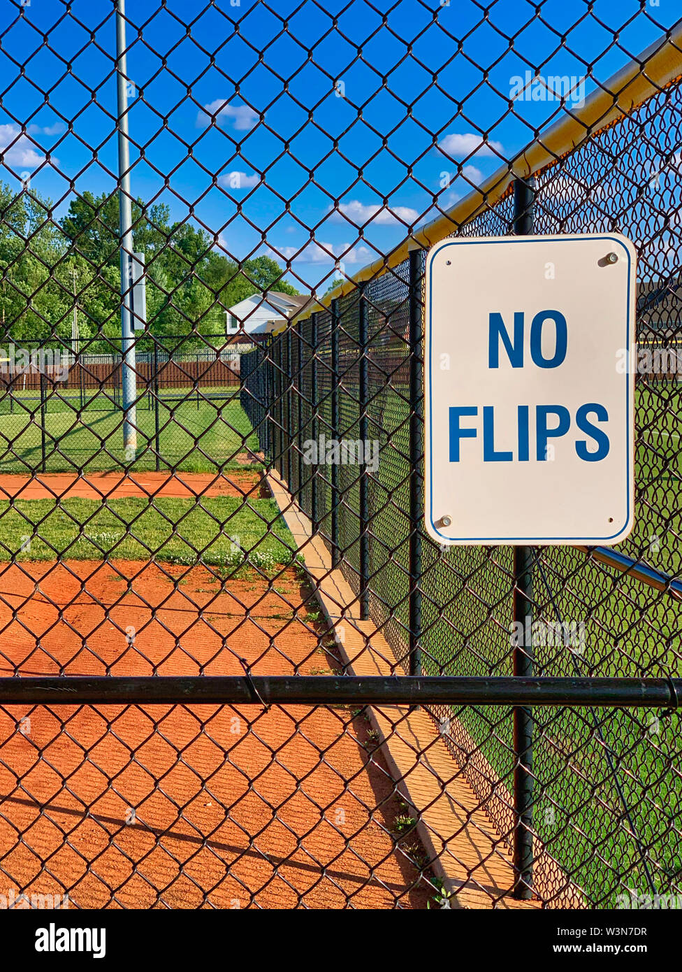 Keine flips Schild an einer kleinen Liga oder Slow Pitch Softball Feld auf einem blauen Himmel mit weißen Wolken Puffy. Von der Innenseite der Einbaum genommen. Mit Blick auf Stockfoto