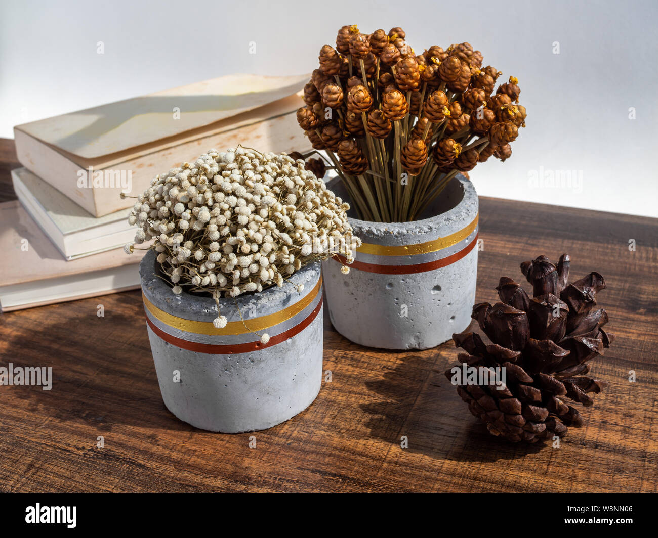 Wunderschön bemalte konkrete Pflanzmaschine mit getrockneten Blumen, natürliche Tannenzapfen und alte Bücher über Holz- Hintergrund. Handgefertigte Zement Topf für Dekoration. Stockfoto