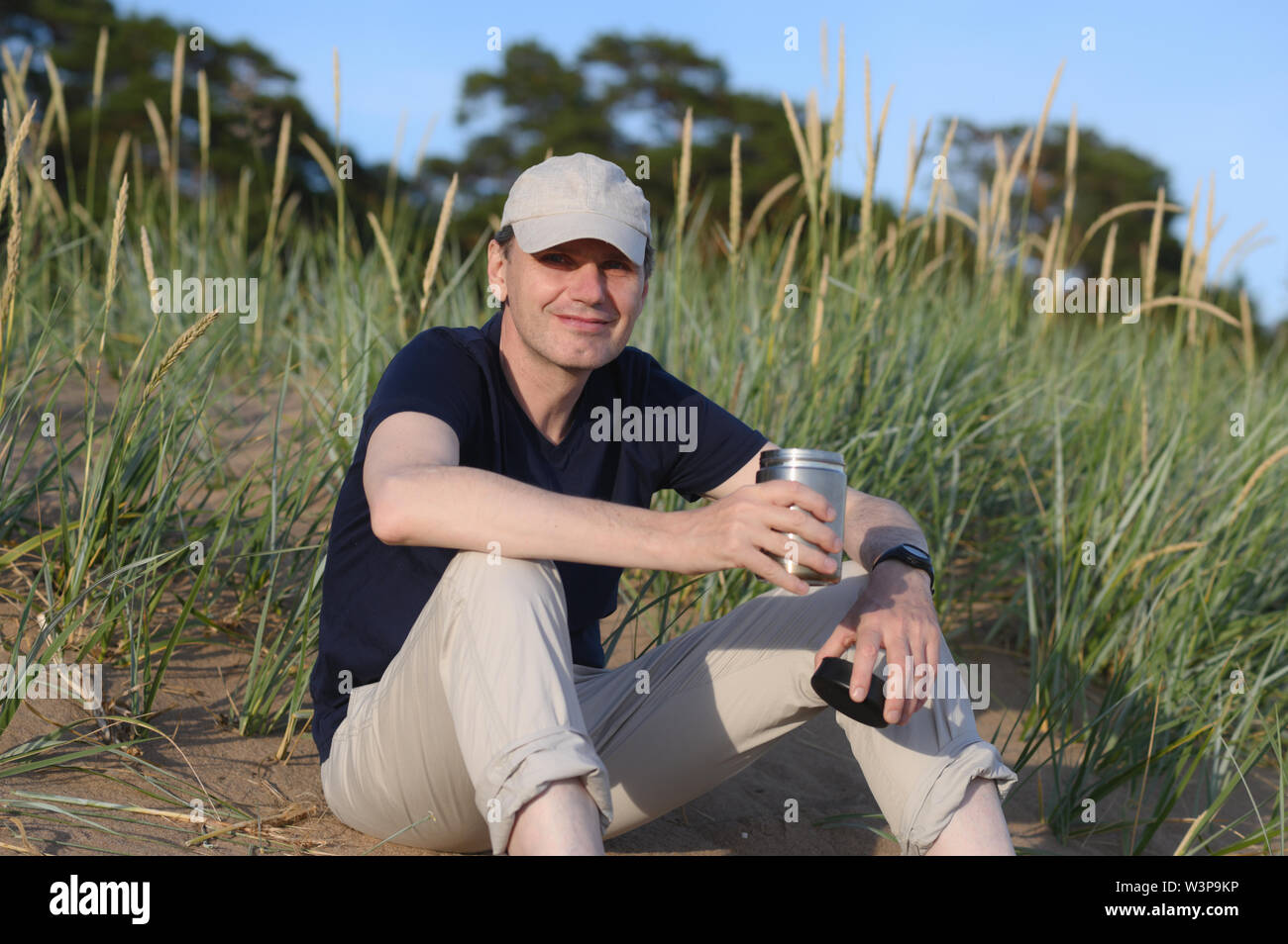 Glücklich Mann sitzt auf einer Düne mit einer Kaffeetasse Stockfoto