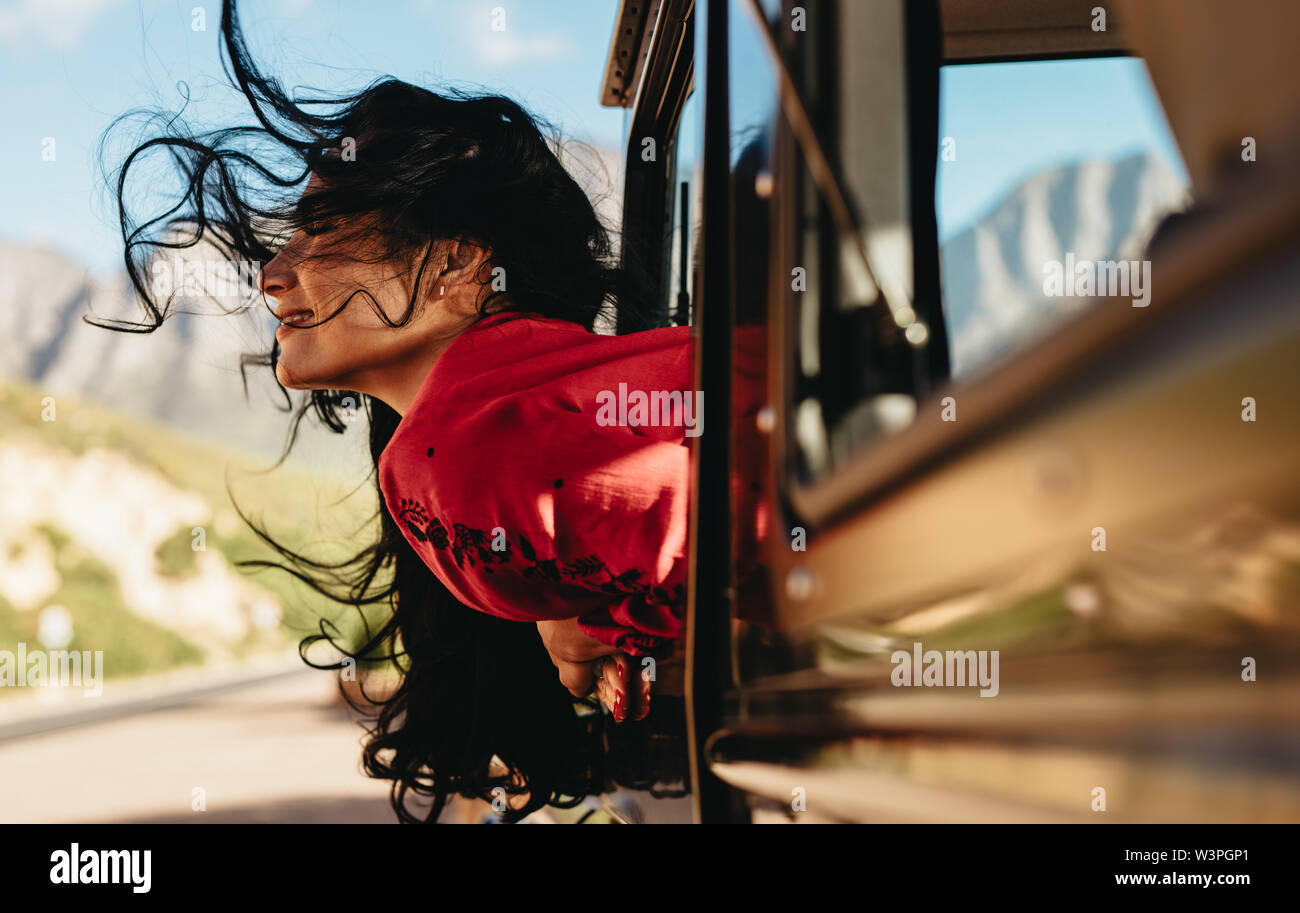 Schöne Frau sitzen auf Auto mit ihrem Gesicht aus dem Fenster mit Ihrem Haar fliegen in der Luft. Weibliche genießen die Fahrt mit dem Auto auf einen Road Trip. Stockfoto