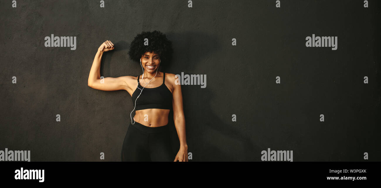 Junge fitness Frau Muskeln und lächelnd. Afrikanische weibliche model in Sportkleidung ihre Muskeln gegen grauen Hintergrund angezeigt. Stockfoto