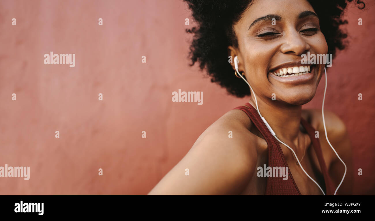 Happy Läuferin gegen braunen Hintergrund lächelnd. Afrikanische Frau mit Kopfhörer lächelnd nach dem Workout. Stockfoto