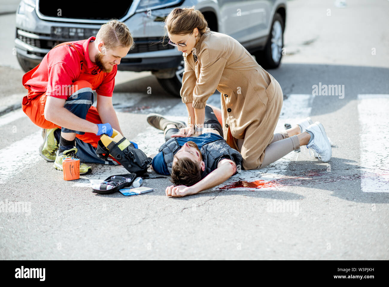 Frau mit ambluance Arbeiter, künstliche Beatmung für die Geschädigte blutender Mann liegen auf dem Fußgängerüberweg nach dem Verkehrsunfall Stockfoto