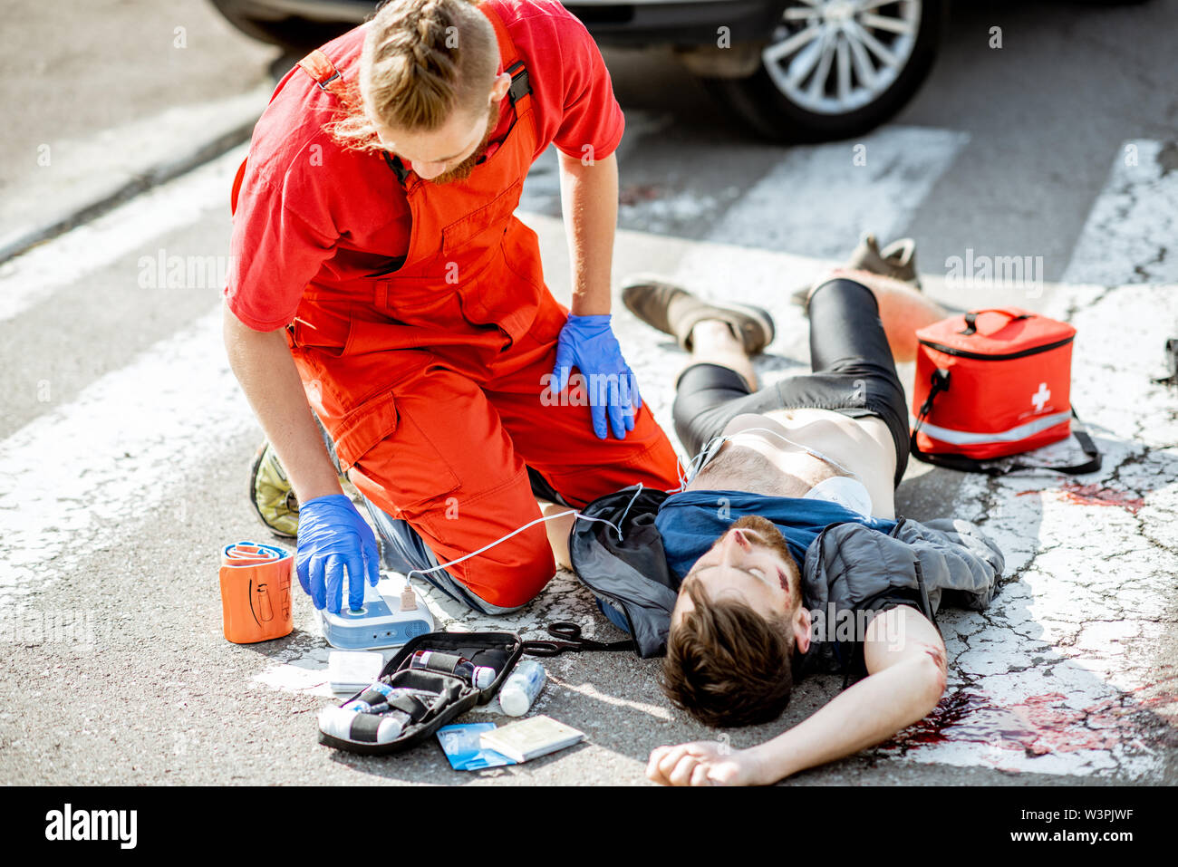 Ambluence Arbeiter, die Notfallversorgung mit Defibrillator auf den Verletzten blutender Mann liegen auf dem Fußgängerüberweg Stockfoto