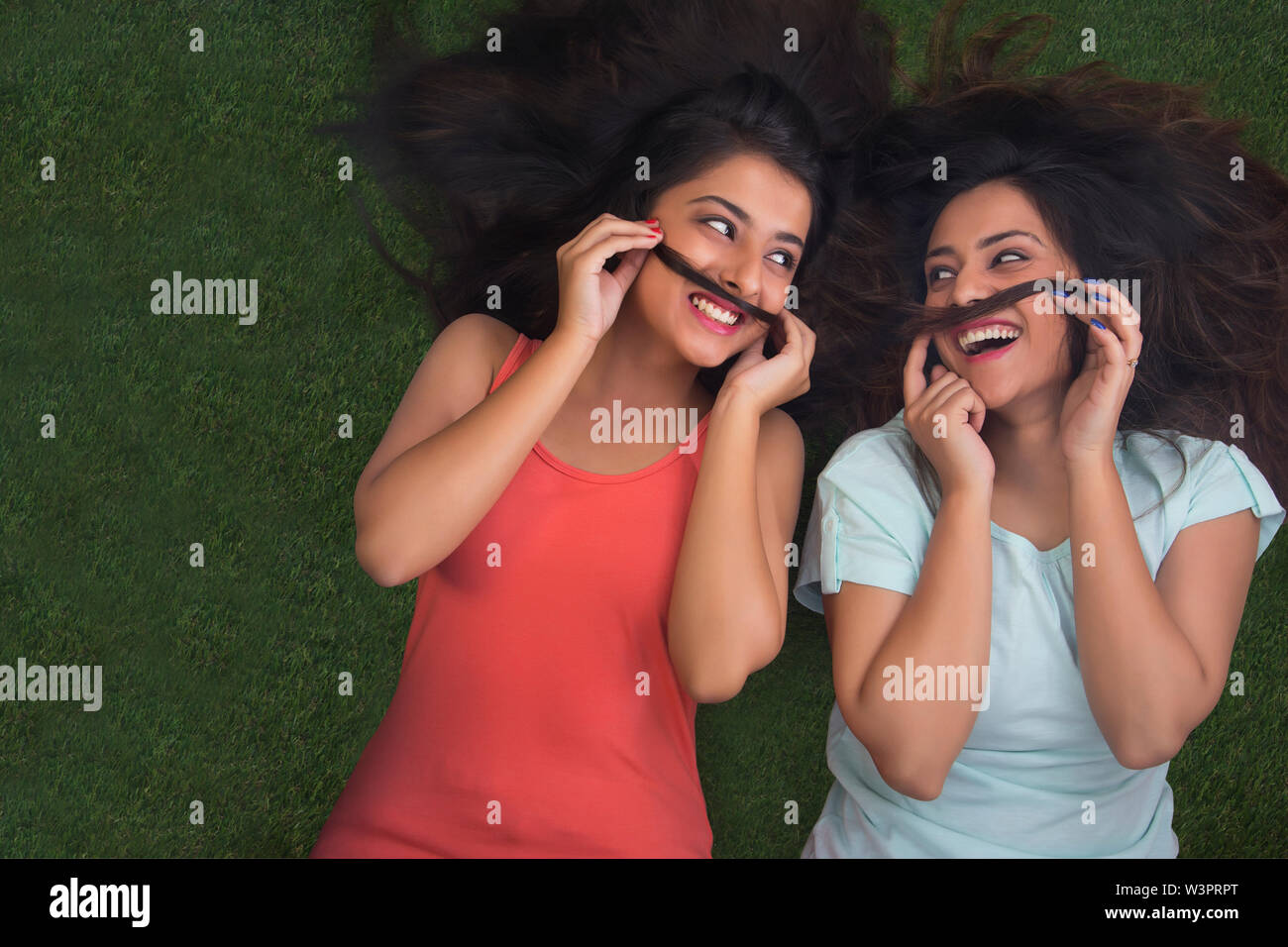 Blick von oben auf die beiden halbwüchsigen Mädchen liegen auf Gras und Schnurrbärte mit ihrem Haar lachend und an jedem anderen Suchen Stockfoto