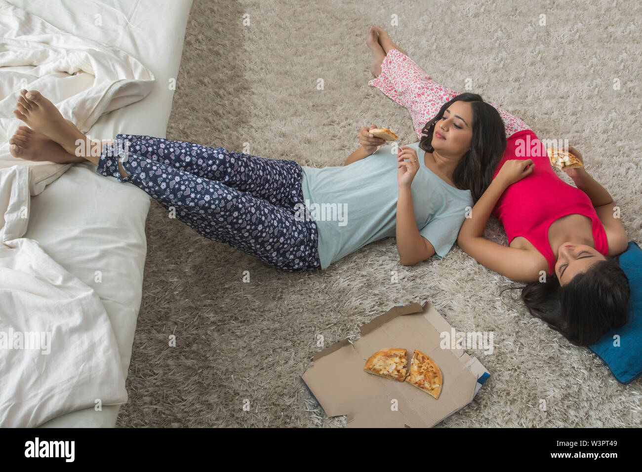 Blick von oben auf die beiden jungen Mädchen auf dem Boden liegend in Haus und essen Pizza gemütlich Stockfoto