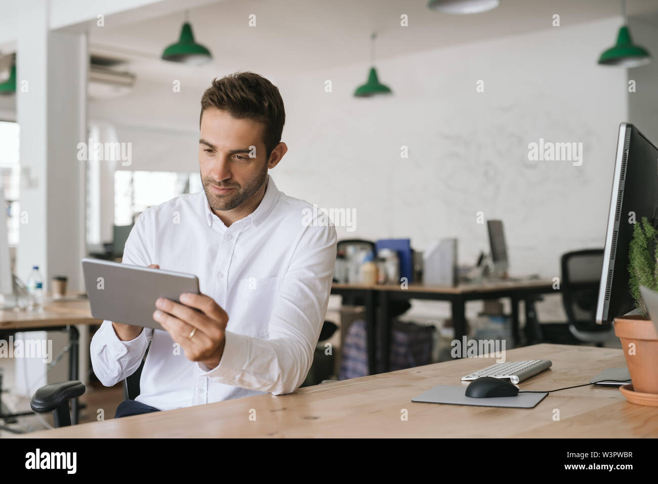 Junge Unternehmer an seinem Schreibtisch sitzend mit einem digitalen Tablet Stockfoto