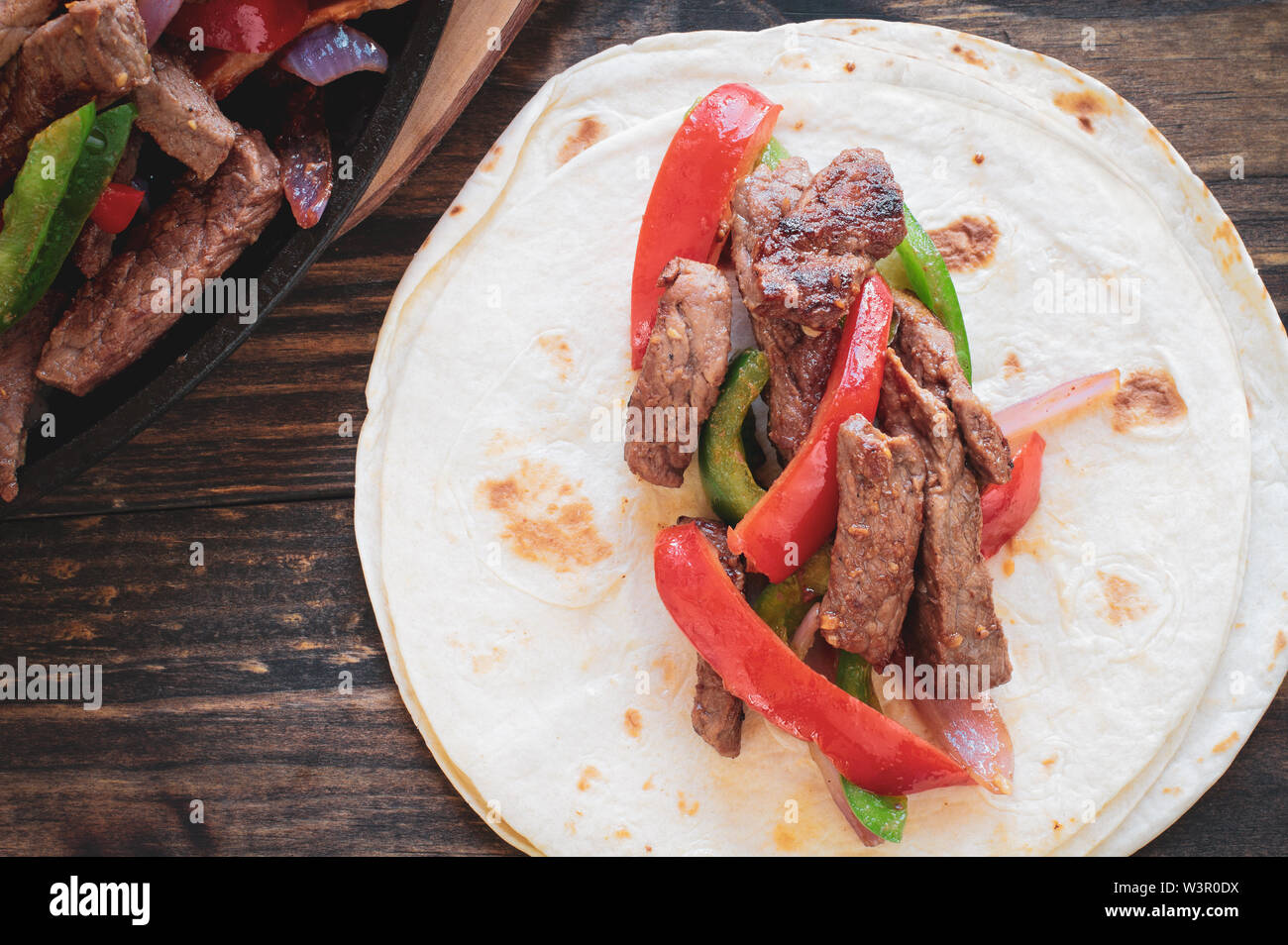 Rindersteak fajita über einem Stapel von Tortilla Wraps mit gusseisernen Pfanne mit frischem heißem Fajita.. Bild geschossen von der Ansicht von oben. Stockfoto