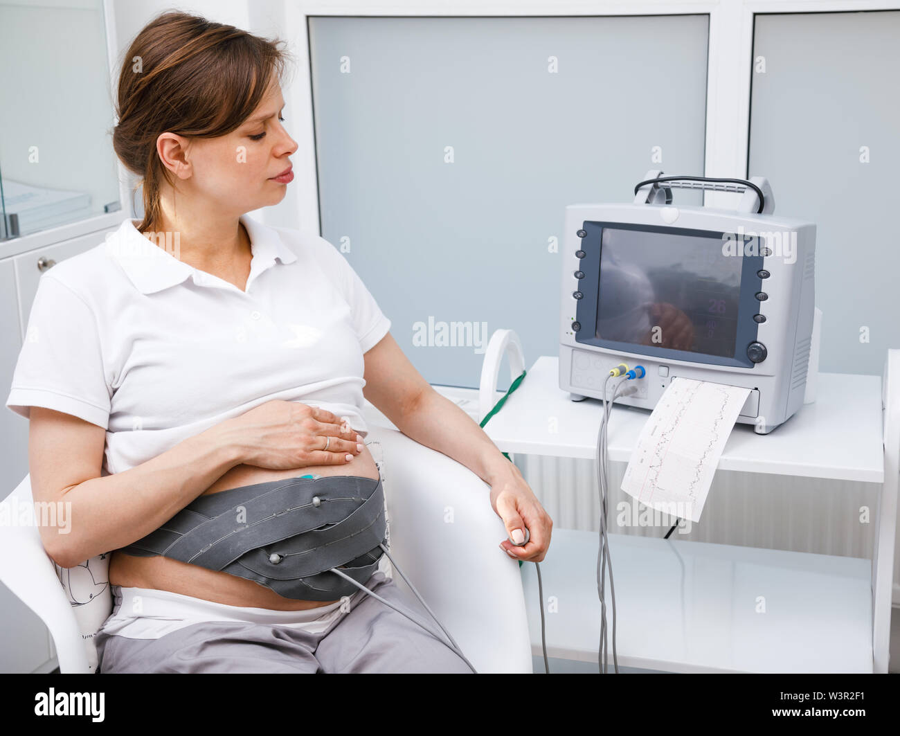 Schwangere Frau in der Klinik sitzen Durchführung cardiotocography (CTG). Den Riemen auf den Bauch mit dem Kardiotokograph Maschine aka Elektronische Feta Stockfoto
