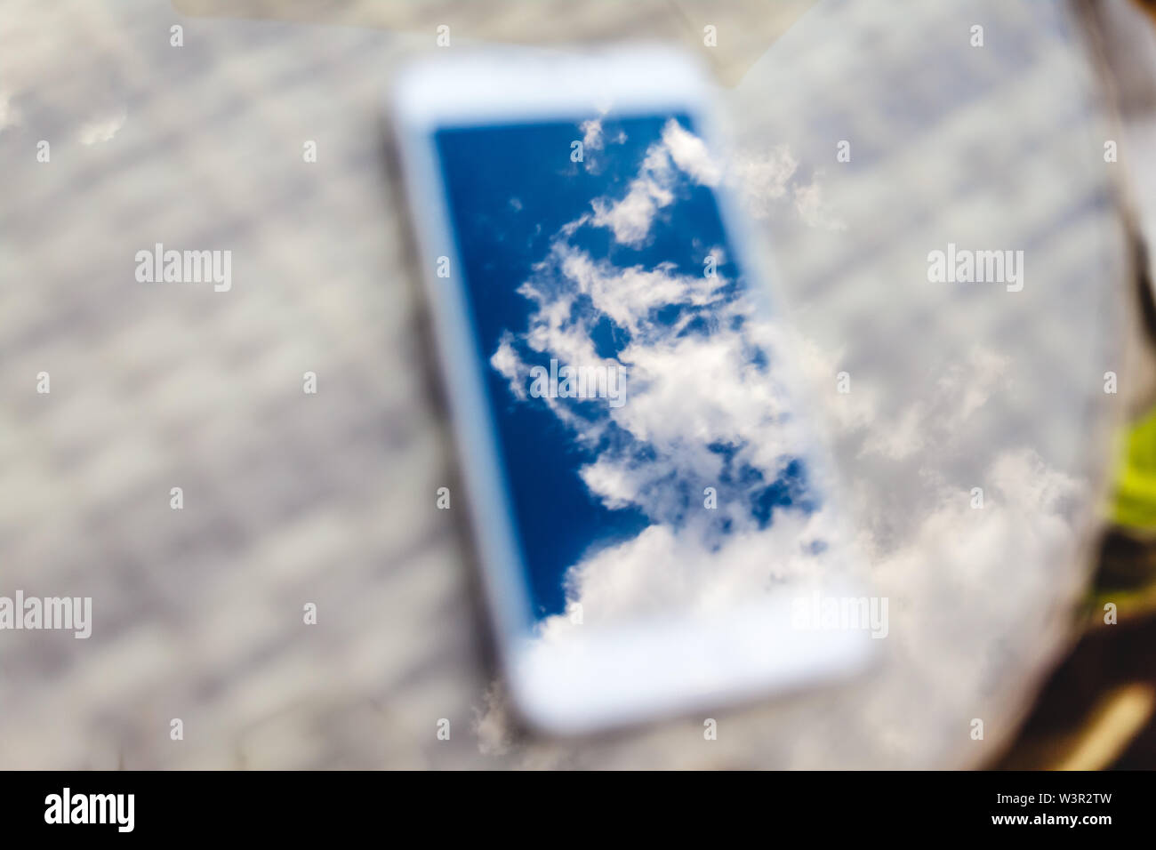 Reflexion der blauen Himmel mit Wolken im Telefon - Smartphone, das auf einem hellen Rattanmöbeln Tabelle vor dem Hintergrund liegt. Blur und Abstraktion Stockfoto