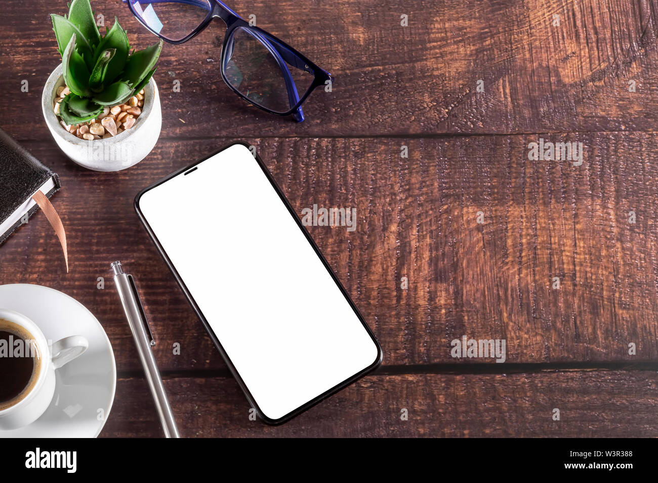 Arbeitstisch mit Smart Phone Editor Kaffee Tasse Kugelschreiber Gläser Anlage auf hölzernen Tisch Stockfoto