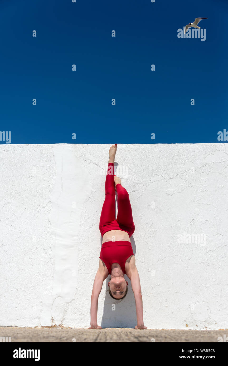 Frau macht Handstand gegen eine weiße Wand mit einem blauen Himmel tragen rot. Stockfoto