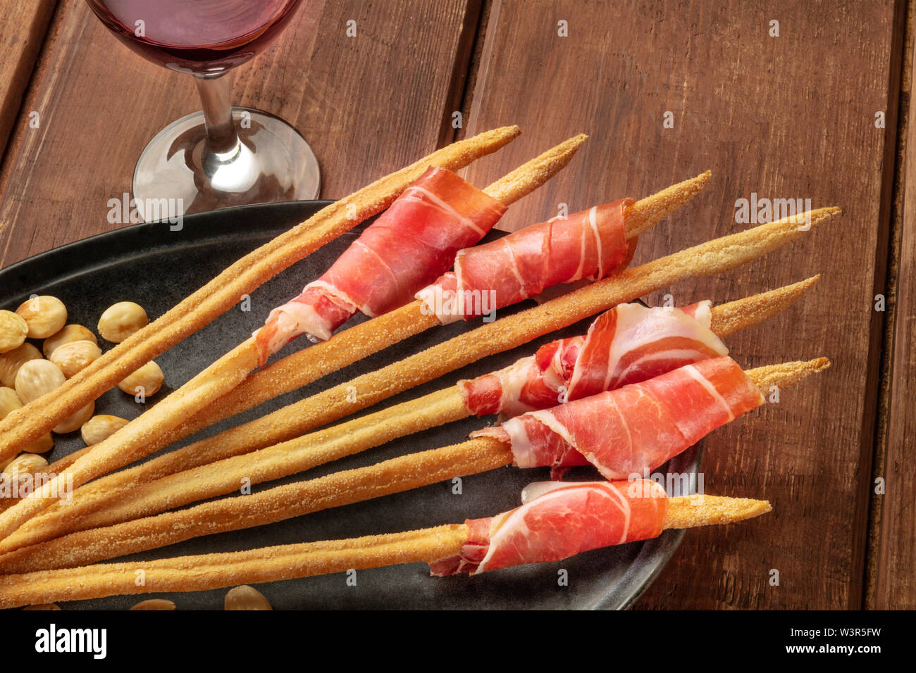 Schinken eingewickelten Italienische Grissini mit rotem Wein und gerösteten Mandeln, Nahaufnahme auf einer hölzernen Hintergrund. Italienische Antipasti mit Parmaschinken Stockfoto
