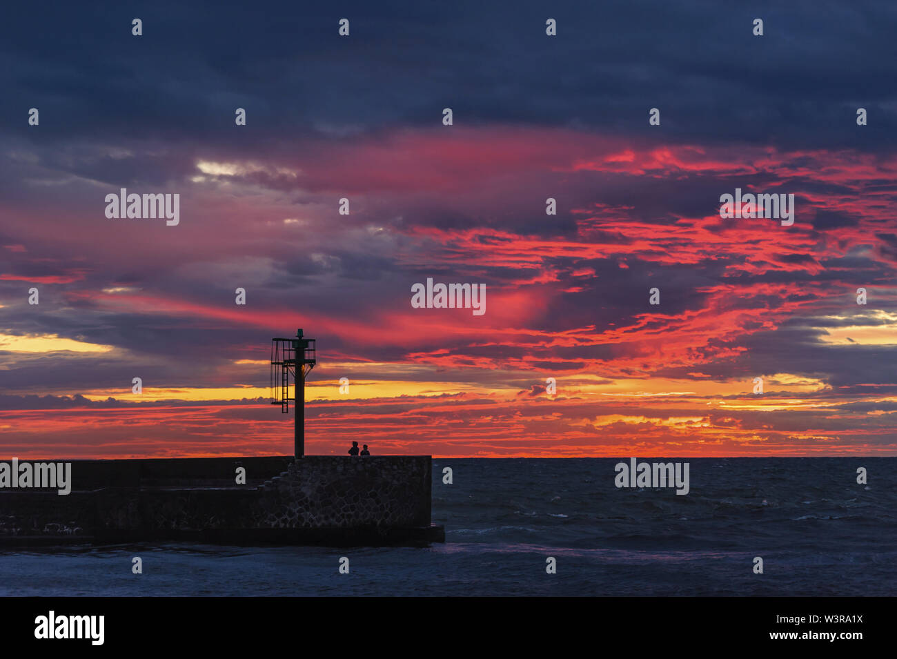 Sonnenuntergang am Meer mit Silhouetten, die auf der Mole Stockfoto