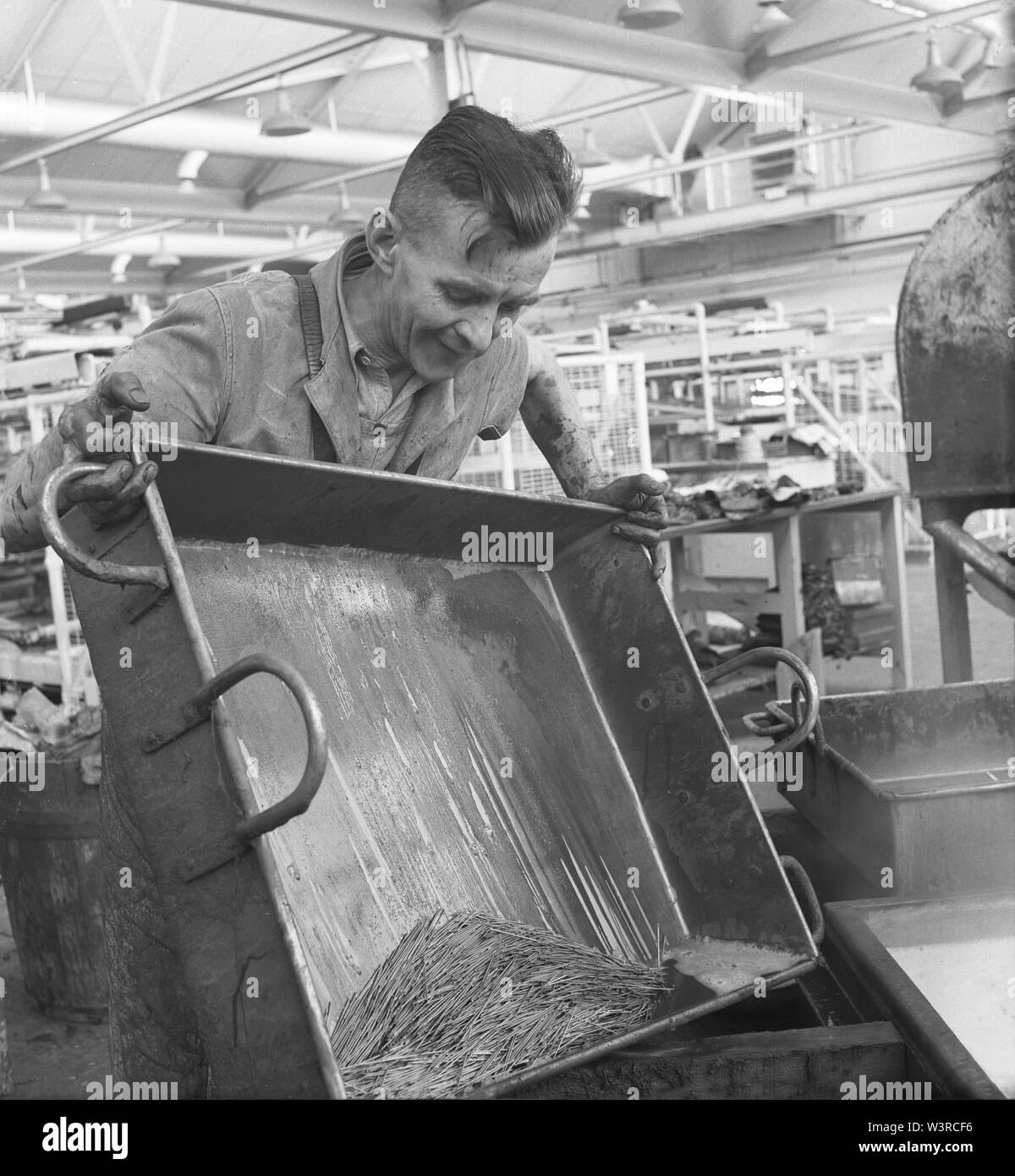 1950er Jahre, historisch, Fertigung, männliche Arbeiter hält ein Metalltablett mit einer großen Menge von Stahl Engineering Pins, England, Großbritannien. Stockfoto
