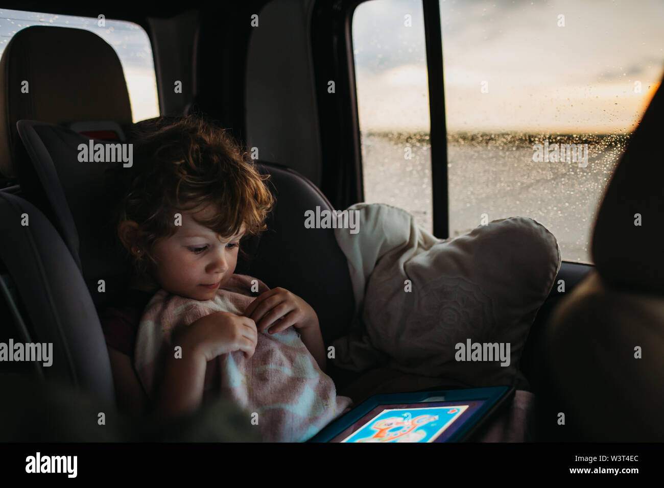 Junge Mädchen spielen Lernspiel auf der Fahrt mit dem Auto nach Hause, während es regnet Stockfoto