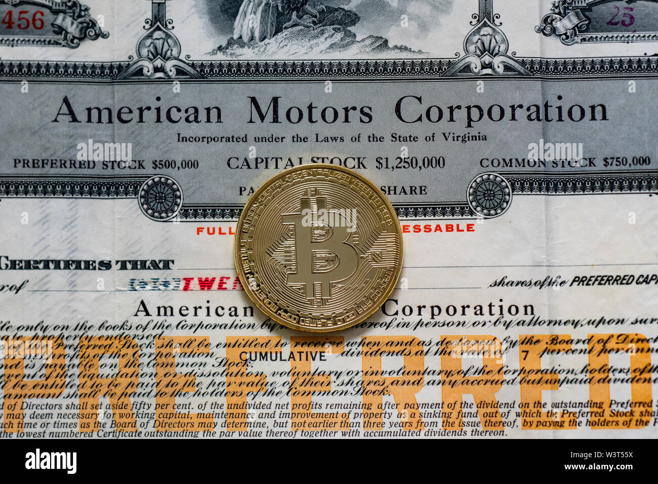 Eine goldfarbene Bitcoin auf einem alten Vorzugsaktien Zertifikat von American Motors Corporation, ein Vergleich von Wert und Gefahr für die Finanzmärkte. Stockfoto