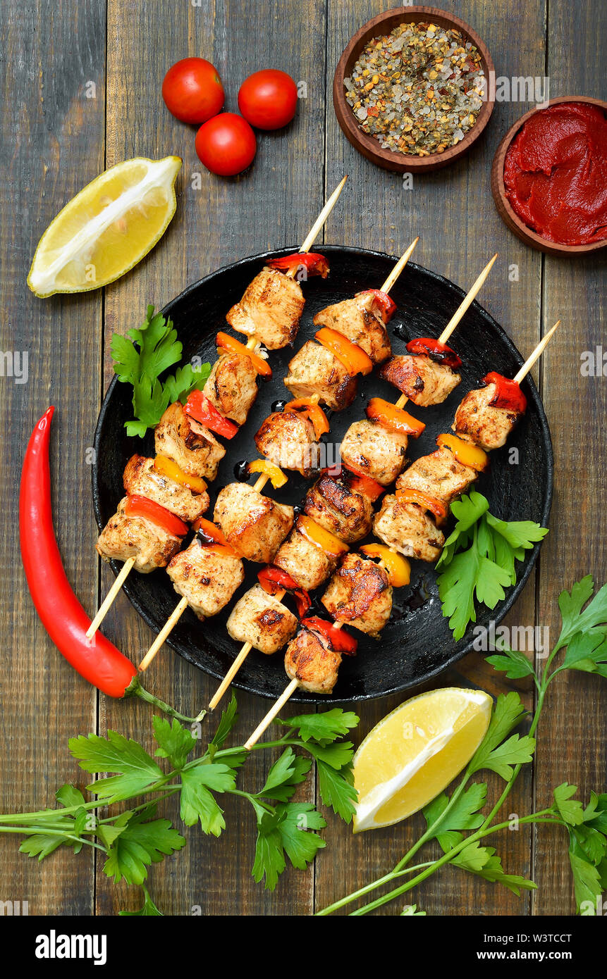 Gegrilltes Hühnchen Kebab mit Paprika in der Pfanne, Gemüse und Kräutern auf Holztisch, Ansicht von oben Stockfoto