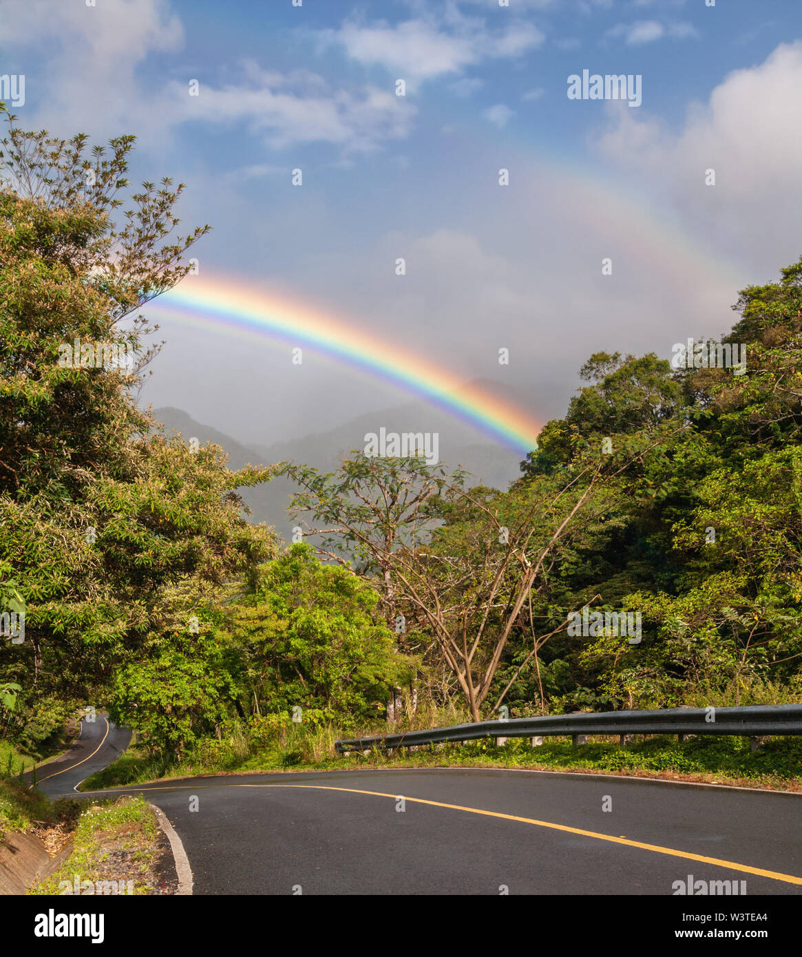 Intensiver Regenbogen, eine schmale Straße inmitten üppiger Vegetation in Boquete, einer Stadt im Hochland von Westpanama. Stockfoto