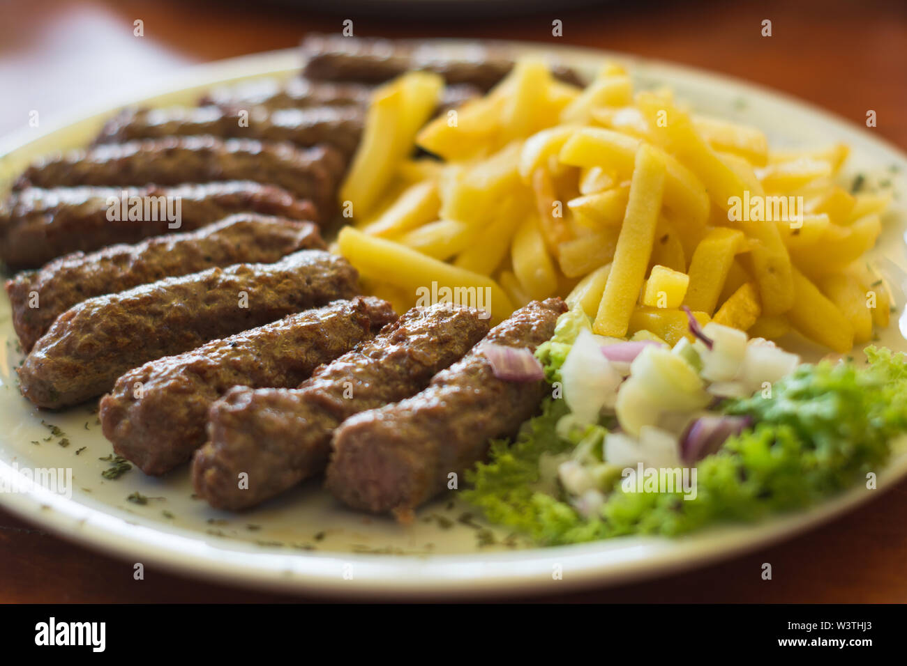 Cevapi, traditionelle serbische Spezialität mit Pommes frites, Salat und Zwiebeln Stockfoto