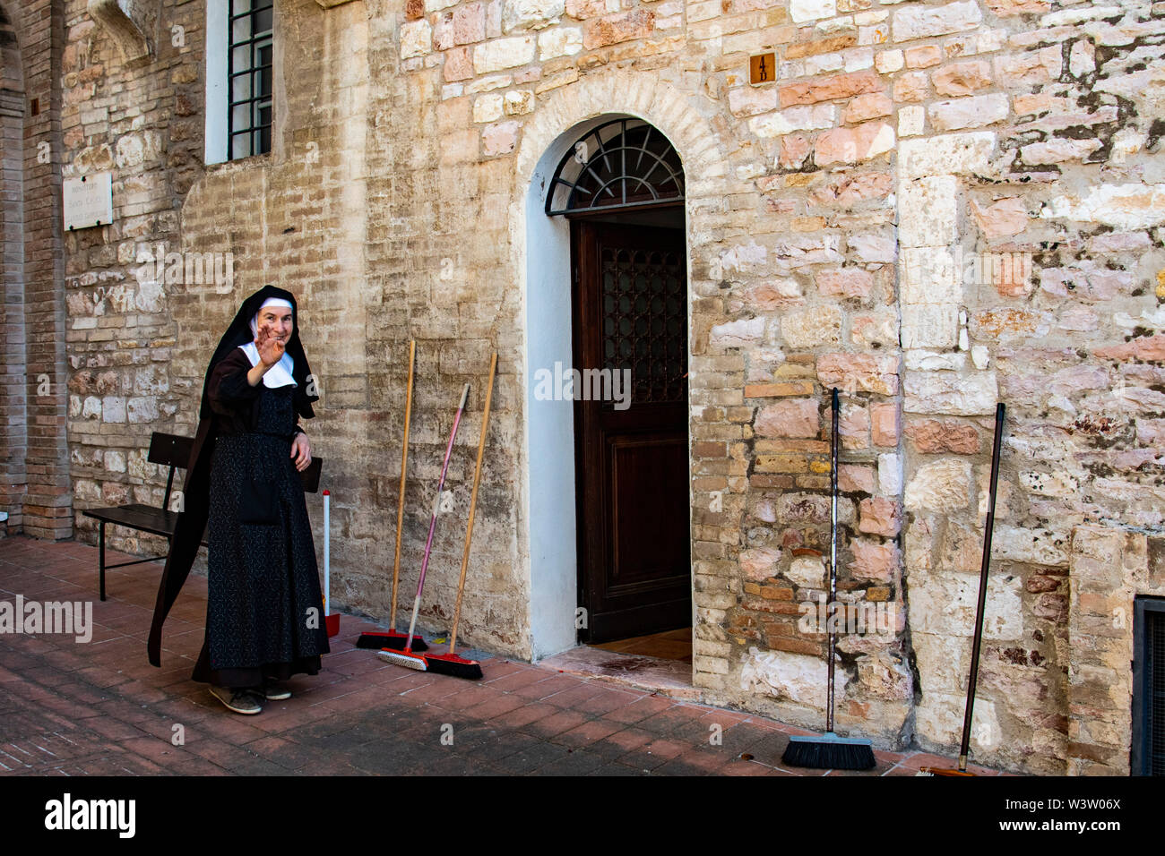 Eine Nonne nimmt einen Bruch von Reinigung und lächelt und Wellen außerhalb Ihres Wohnsitzes in Assisi, Italien Stockfoto