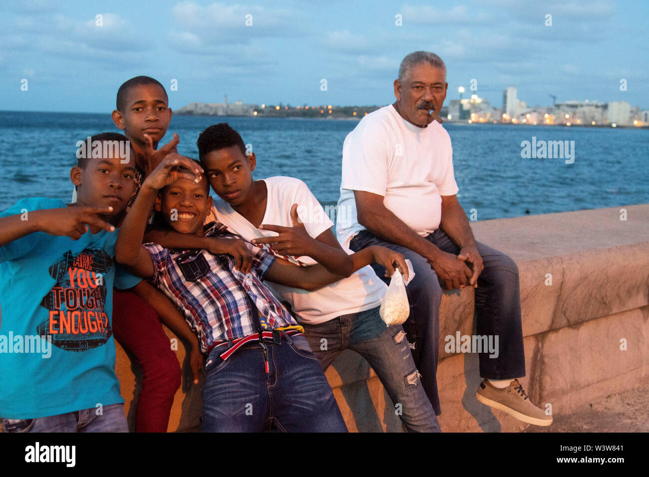 Ein älterer Mann mit einer Gruppe von jungen Kindern eine gute Zeit auf dem Malecon in Havanna, Kuba sitzen Stockfoto