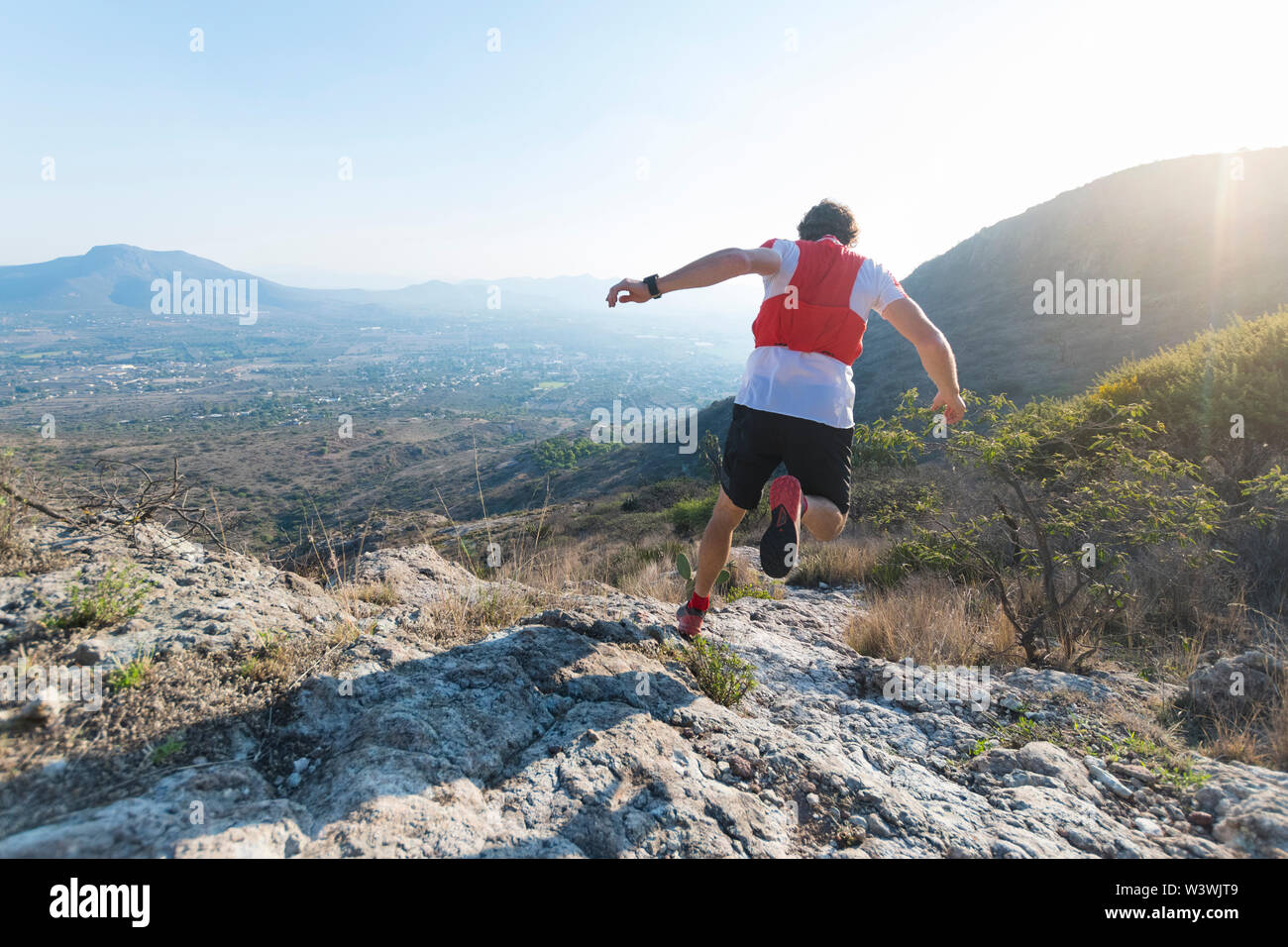 Eine starke, atheletic Mensch ist von hinten gesehen, wie er hinunter läuft Full Tilt auf einer trockenen, felsigen Trail in den Bergen von El Arenal, Hidalgo, Mexiko, als s Stockfoto