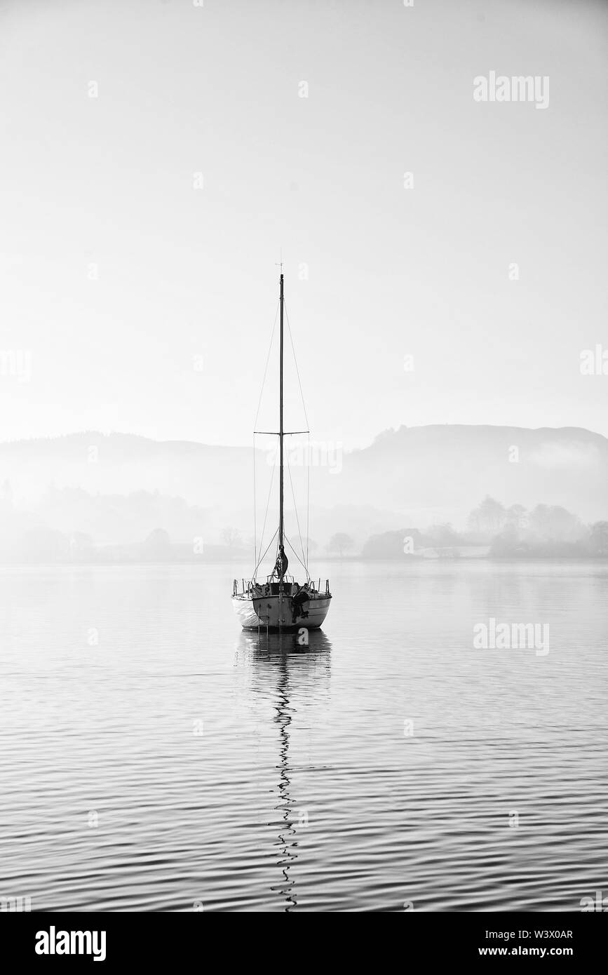 Schöne unplugged Landschaft Bild der Segelyacht sitzt immer noch in ruhigen See Wasser im Lake District während der friedlichen nebligen Herbst Sonnenaufgang Stockfoto